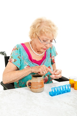 Disabled senior woman in wheelchair counting her pills into a pill container for the week   White background   の写真素材