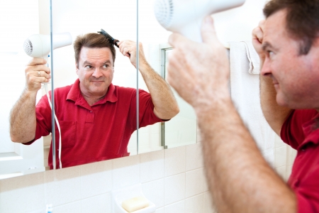 Man drying his hair with a hand held blow dryer in the bathroom mirror   の写真素材