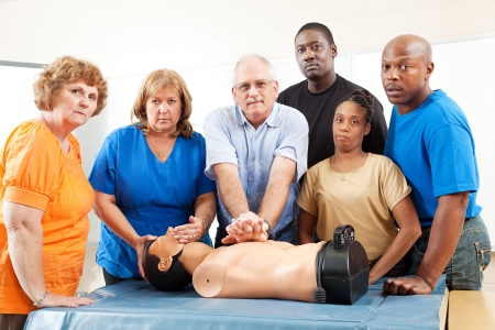 Diverse adult education class practicing CPR on a mannequin.  Serious expressions