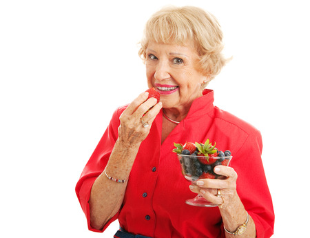 Fit healthy senior woman biting into a strawberry and holding a bowl of mixed berries.  の写真素材