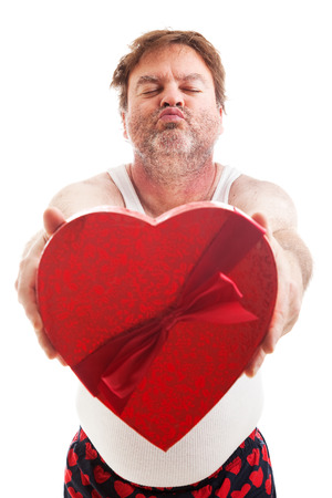 Humorous photo of a scruffy looking middle aged man in his underwear holding a box of Valentines day candy and waiting for a kiss. Isolated on white.の写真素材