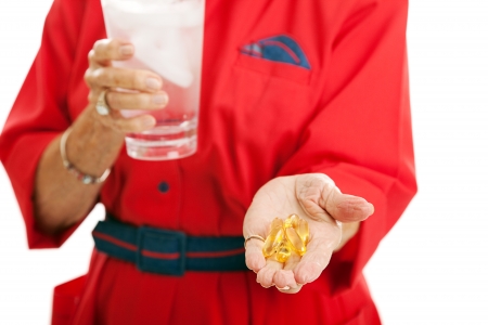 Senior woman taking omega 3 fish oil capsules for health.  Closeup with focus on the fish oil in her hand.  の写真素材