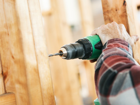 Closeup of a carpenter's hands using a drill on a construction site.  Focus on drill and hand.  Shallow depth of field.の写真素材