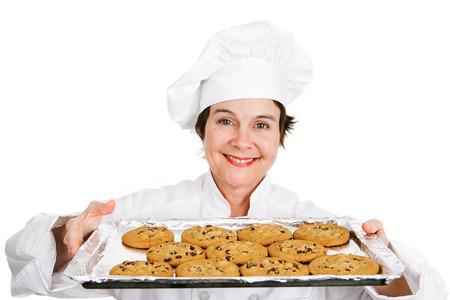 Cute female chef in her uniform, holding up a tray of delicious, freshly baked chocolate chip cookies.  Isolated on white background.の写真素材