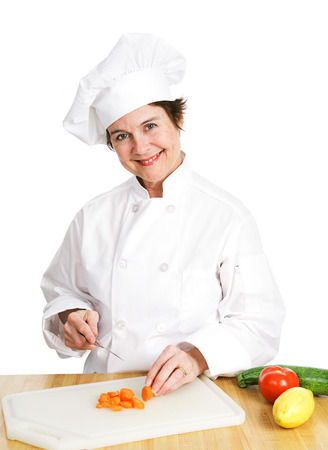 Petty female chef in her uniform, cutting up a variety of fresh organic vegetables on her cutting board in the kitchen.  Isolated on white background.の写真素材