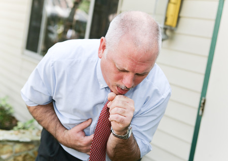 Mature businessman with gray hair, doubled over with a bad cough from a cold, flu, or ebolaの写真素材