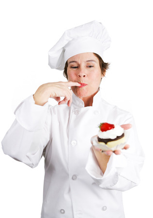 Pretty pastry cook in chef's whites tasting a delicious chocolate cheesecake tart with whipped cream and a cherry on top.  Isolated on white background.の写真素材
