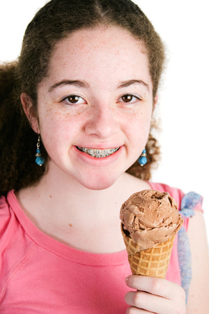 Portrait of cute Latina girl with curly hair and braces holding a yummy chocolate icre cream cone.  White background.の写真素材