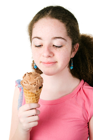 Pretty hispanic teen girl with curly hair and freckles looking at a yummy chocolate ice cream cone.  Isolated on white.の写真素材