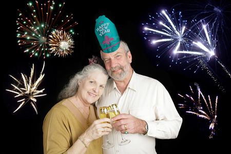 Beautiful senior couple celebrating a Happy New Year with a champagne toast, while fireworks go off in the background.の写真素材