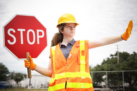 Female construction apprentice holding a stop sign and directing traffic.の写真素材