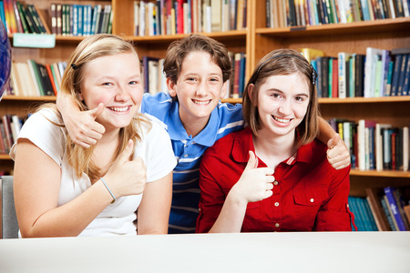 Three school kids giving thumbs up in the library.の写真素材