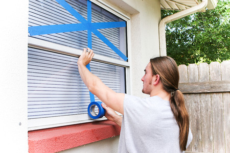 Young man taping up windows in preparation for a hurricane.の写真素材