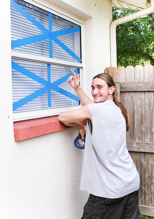 Young man pointing to windows he has taped up to prepare for a hurricane.の写真素材