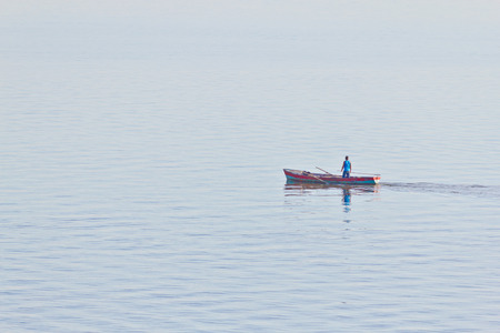 Man fishing at Guaiba lake. Boat and man reflection can be seen.