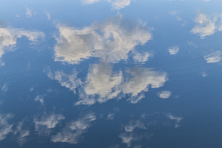 Waves in a lake reflecting sky with cloudsの写真素材