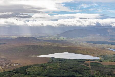 Clouds and sun rays covering valley with lake and forest taken from Croagh Patrick mountain, Westport, Irelandの写真素材