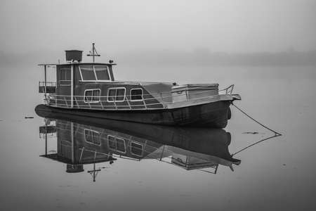Small ship in black and white on a river with fogの写真素材