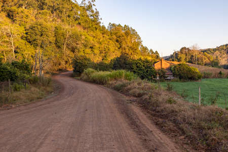 Dirty road and Farm at sunrise with mountain and forest, Santa Cruz do Sul, Rio Grande do Sul, Brazilの写真素材