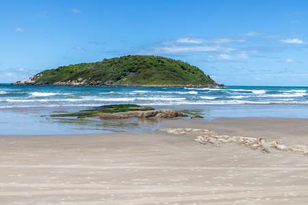 Beach view with sand, rocks, waves and island in background, Barra do Ibiraquera, Ibiraquera, Santa Catarina, Brazilの写真素材