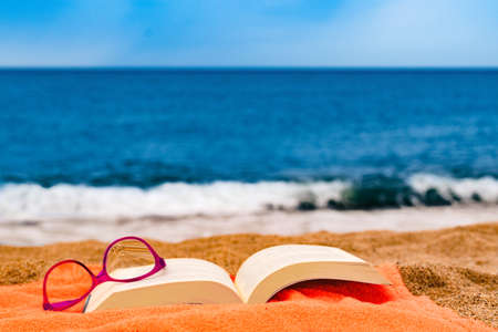 book and glasses on the beach towel with the sea in the backgroundの写真素材