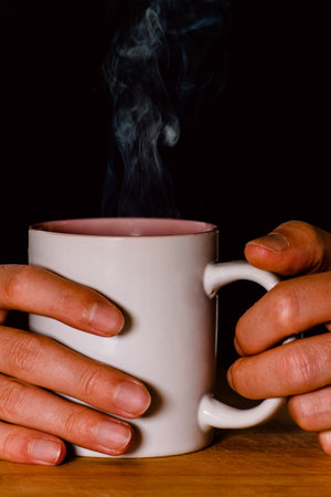 cup with steaming beverage held by two hands on black background