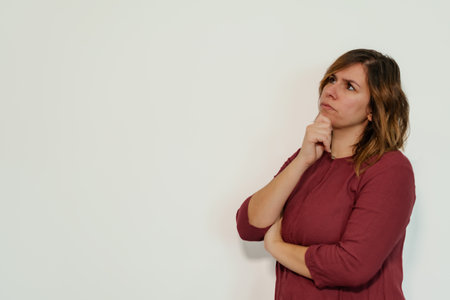 pensive woman with her hand on her chin looking up on white background with copy spaceの写真素材