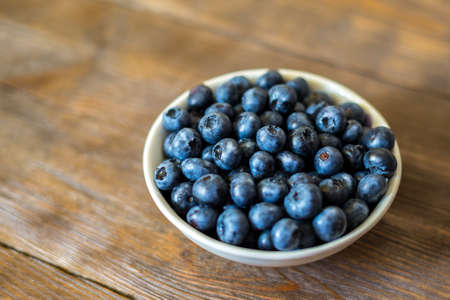 Blueberries on vintage wooden background. Freshly picked berries in white bowl. Ripe and juicy fresh picked bilberries close up. Copyspace for your text. Concept for healthy eating and nutrition.の写真素材