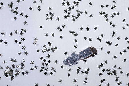 Glass bottle with silver sparkles on a white background with silver stars. Magic backdrop with glitter. Minimalism concept. Top view.の写真素材