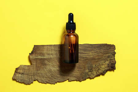 Brown serum or oil glass mock up bottle with pipette on yellow background. Bark of tree on backdrop....