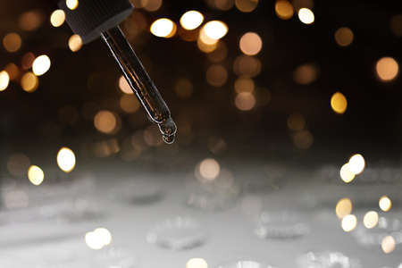 Transparent serum pipette with drops on dark background with gold light blurred and bokeh. Cosmetics greeting concept. Minimalism style and extreme close up.の写真素材