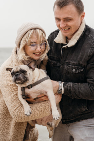 Happy couple playing with their dog. Young man and woman with their pet pug. Outdoors. Lifestyle.の写真素材