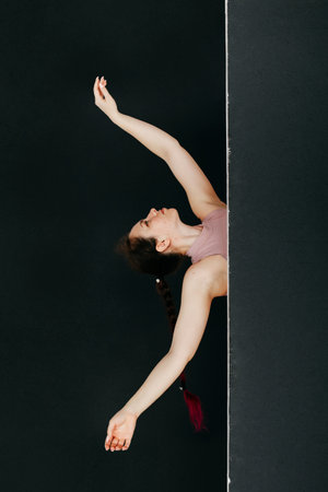 A beautiful brunette peeks out from behind a black screen. Studio portrait of a young woman makes smooth movements with her hands. Concept for cosmetic procedures and manicure.の写真素材