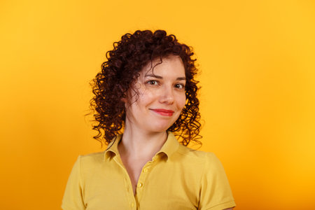 Studio shot of positive and smiling girl. Curly young woman in bright yellow t-shirt. Yellow background.の写真素材
