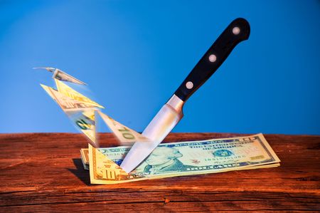 Kitchen knife cutting pieces of from Dollars. Pieces flying away. Blue background.の写真素材