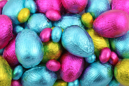 Pile of foil wrapped chocolate easter eggs in pink, blue & lime green.