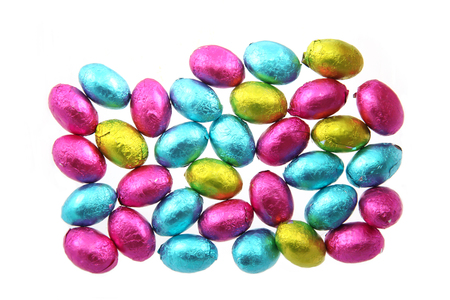 Pile of foil wrapped chocolate easter eggs in pink, blue & lime green with a white background.