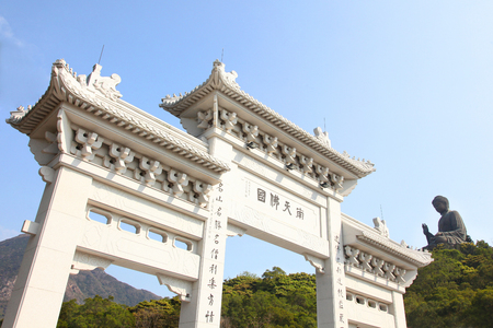 Entrance gate to Tian Tin monastery and the Big Buddha on the mountain behind at Ngong Ping village on Lantau Island, Hong Kong, China.のeditorial素材