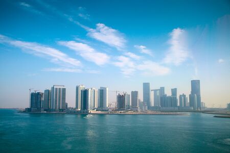 Skyline of the city surrounded by the ocean. Many skyscrappers, & office buildings tower across the landscape, Abu Dhabi, United Arab Emirates.の写真素材