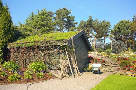Typical garden shed with grass roof, in a beautiful garden with a wheelbarrow, Stavanger, Norway.の写真素材