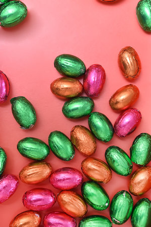 Large and small colorful pink, green, orange and gold foil wrapped chocolate mini easter eggs,...