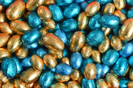 Blue,  gold and turquoise foil wrapped chocolate easter eggs, against a black background.