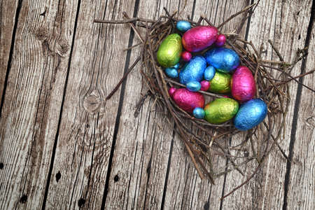 Foil wrapped colourful easter eggs in pink, green, blue and yelow in a natural nest made of sticks...
