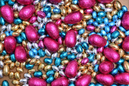 Small pink, blue, silver and gold foil wrapped chocolate easter eggs, with large pink eggs against a...