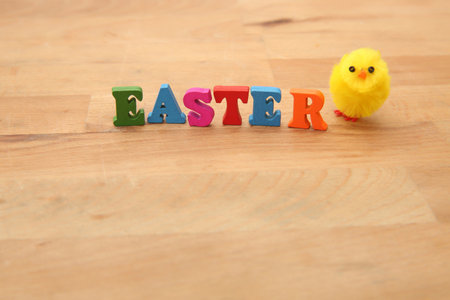 Easter spelt in colourful wooden letters against a natural wooden beige background with a fluffy...