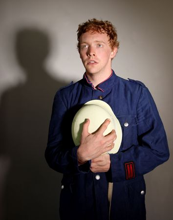 Spotlight on a man in an oldfashioned fireman / firefighter uniform sadly clasping his helmet.の写真素材