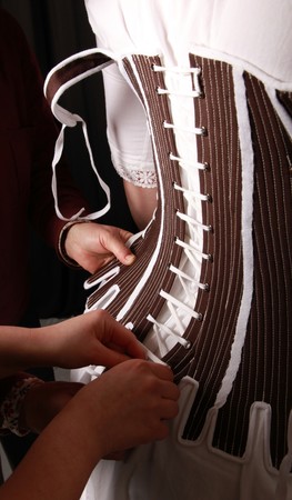 Two women lacing up another in a historical corset.の写真素材
