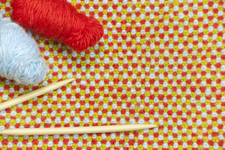 Hanks of red, blue yarn and knitting needles on the background of knitted, woolen cloth