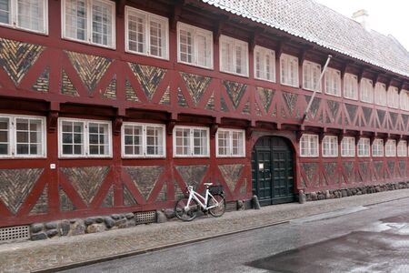 Red old house with white windows - half-timbered house made of wood and bricks. Bicycle near the wall. Denmarkのeditorial素材