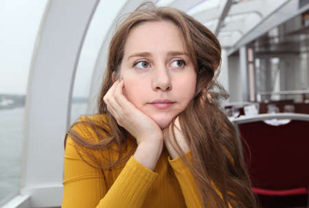 A girl with very long hair in a yellow turtleneck put her face thoughtfully in her arms in a cafeの写真素材